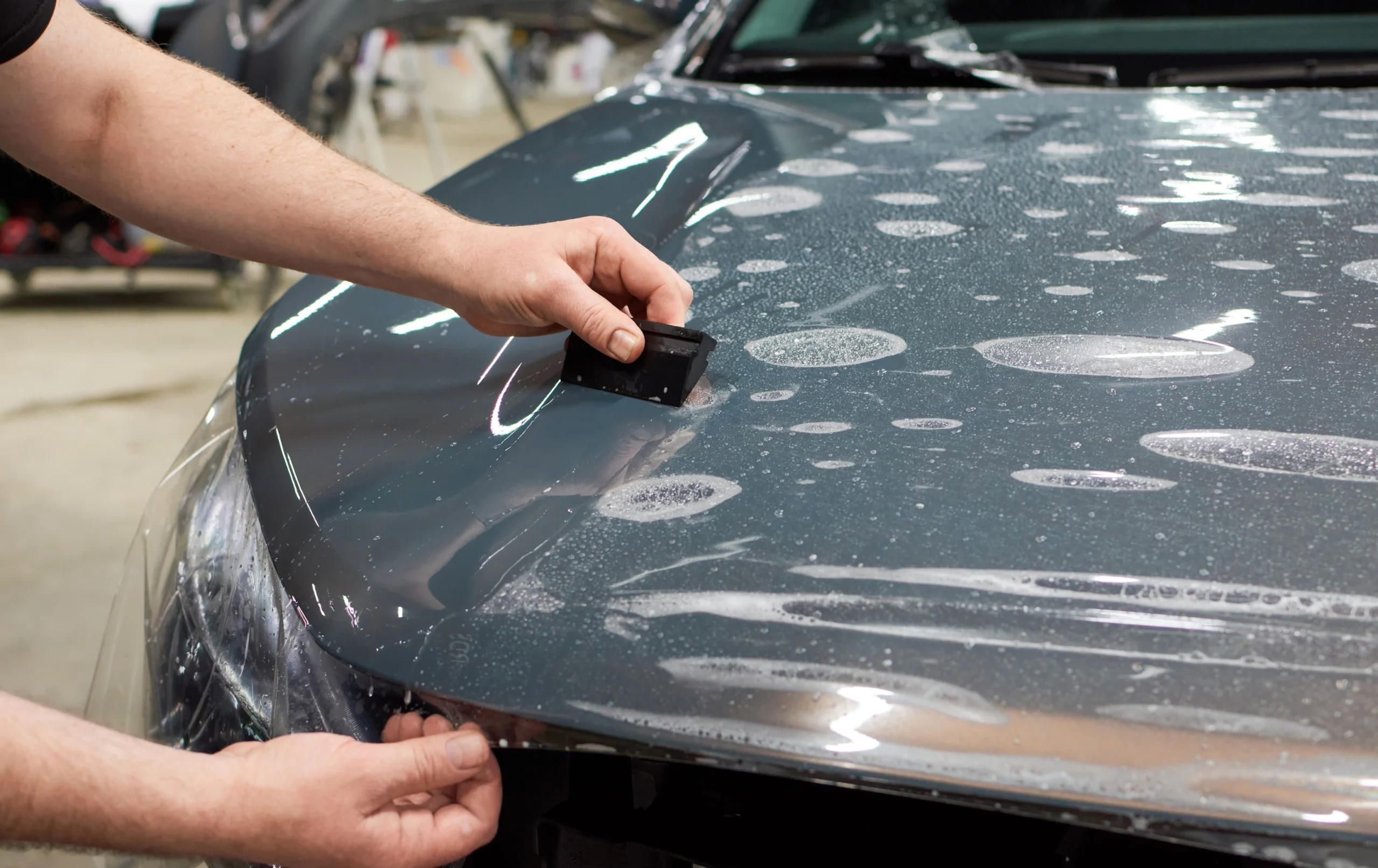 Professional installation of Paint Protection Film (PPF) on car bonnet using squeegee tool